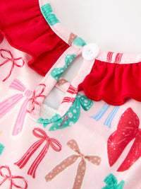 Close-up of a children's top featuring a pink base printed with colorful bow motifs, accented by bright red ruffled trim and a white button closure.