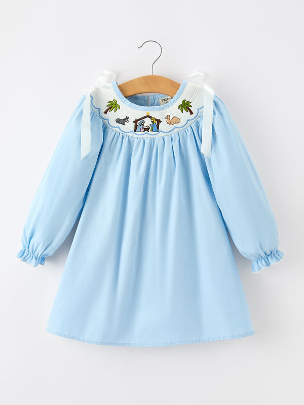 Light blue long sleeve girls dress with smocked neckline featuring embroidered nativity scene, palm trees, animals, and bow shoulder straps.