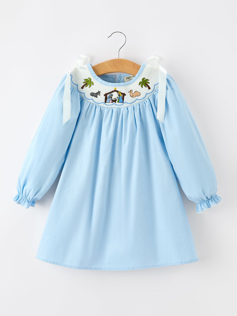 Light blue long sleeve girls dress with smocked neckline featuring embroidered nativity scene, palm trees, animals, and bow shoulder straps.