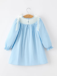 Blue girls Christmas dress with white smocked neckline, long puff sleeves, and white bow shoulder straps.