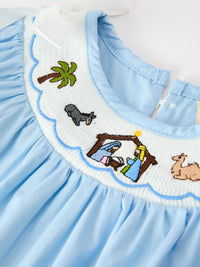 Boca blue baby bubble romper featuring smocked white neckline with embroidered nativity scene, palm tree, and animal motifs.
