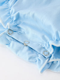 Boca blue baby bubble romper side detail showing silver snap buttons on smocked fabric with white trim.