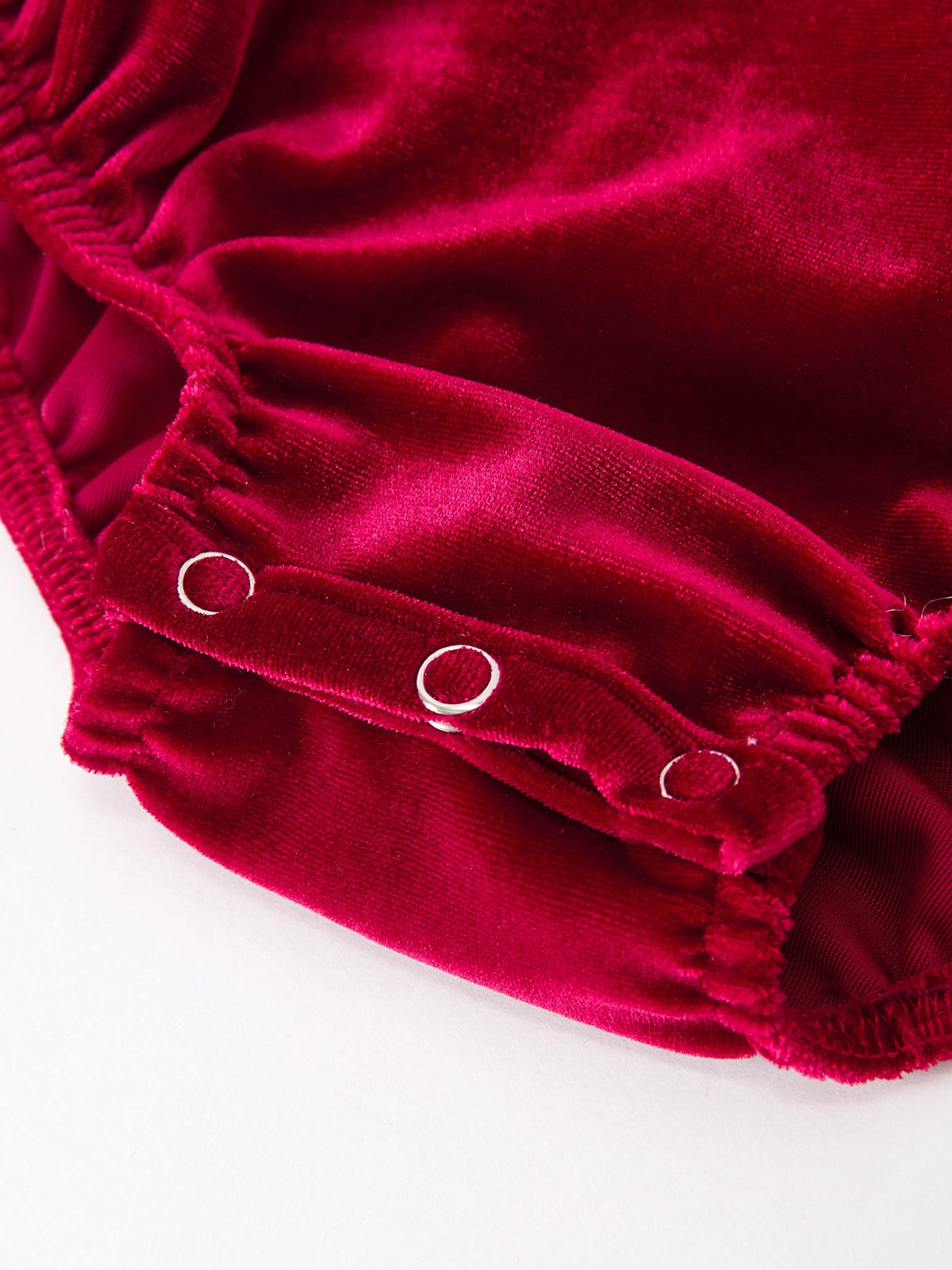 Burgundy velvet baby bubble romper leg detail with silver metal grommets and elasticized ruffle cuff.