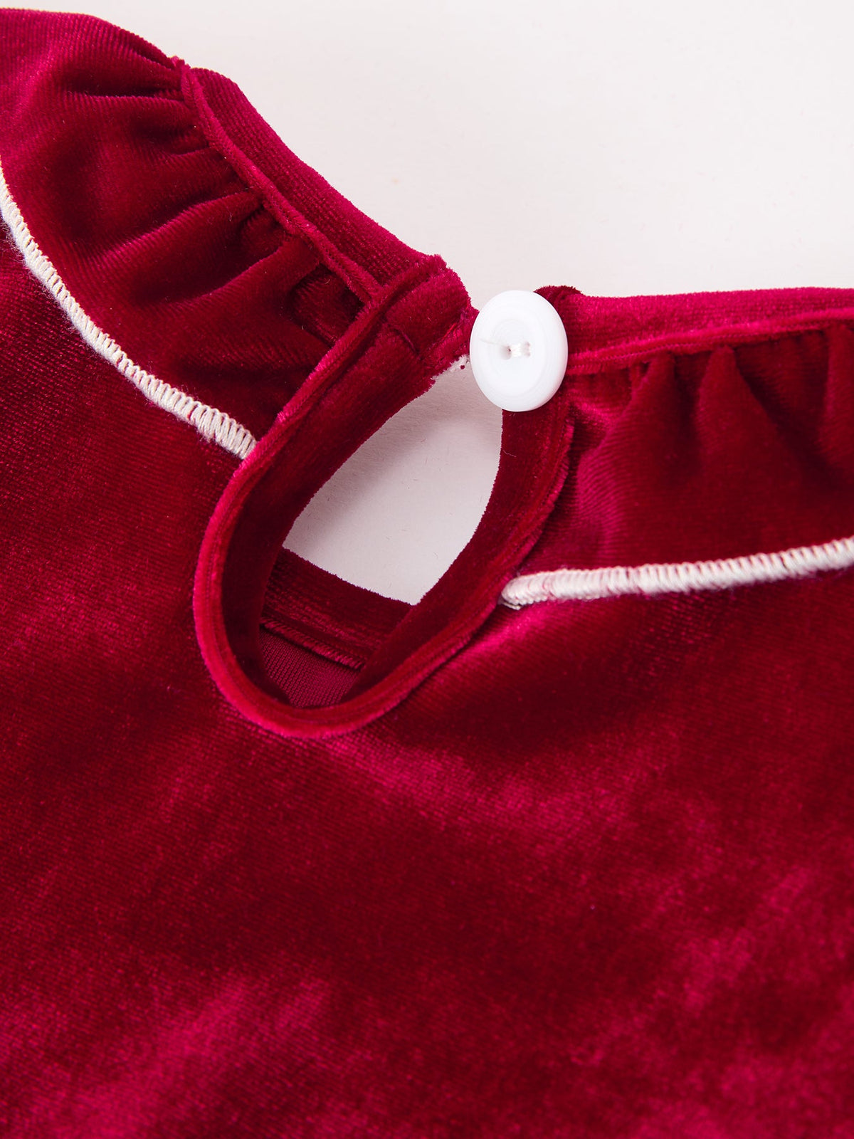 Burgundy velvet baby romper detail showing ruffled collar with white trim and white button closure.