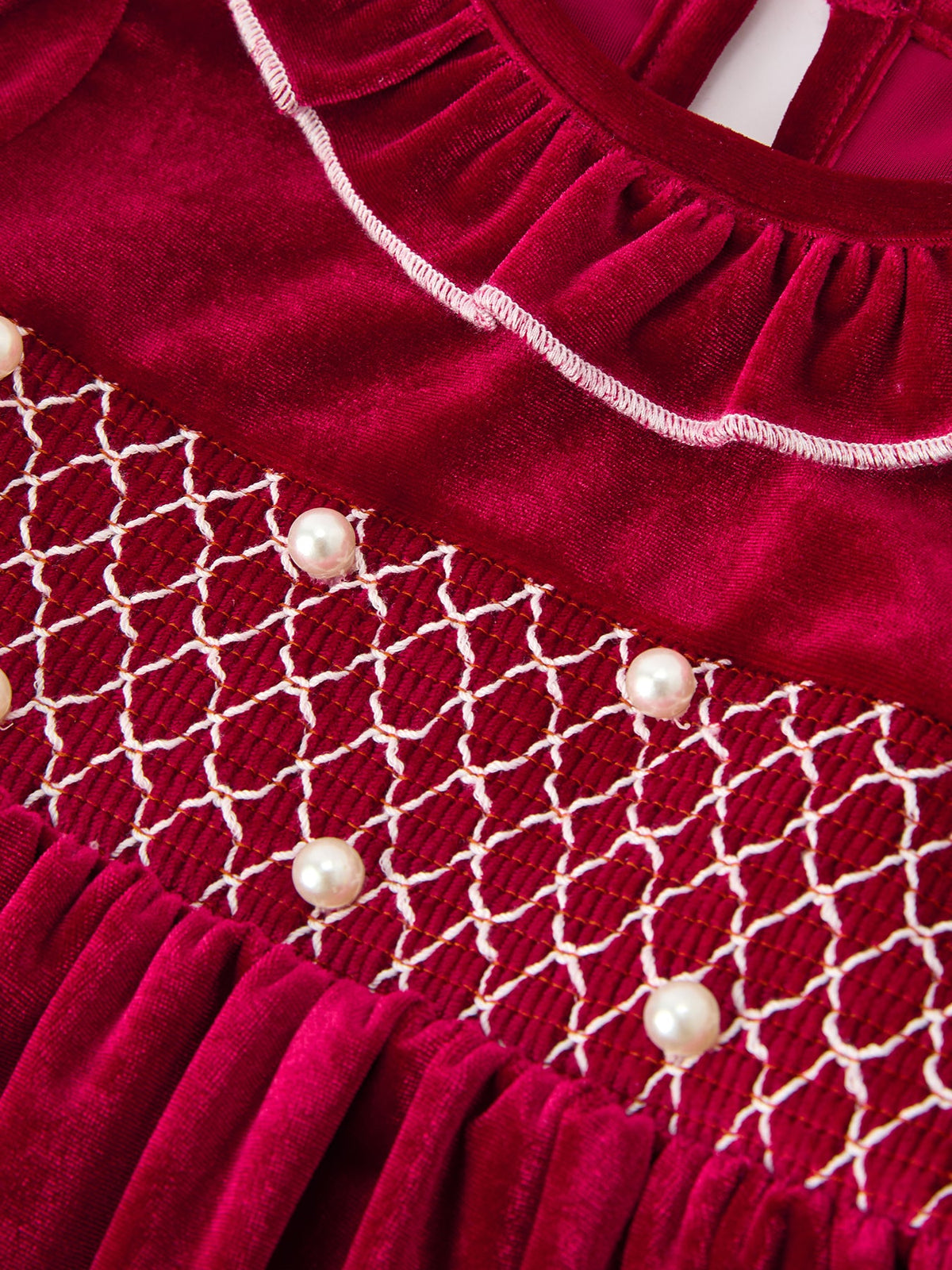 Burgundy velvet girls dress featuring white smocked waist detail, pearl accents, and delicate ruffle neckline for the holiday season.