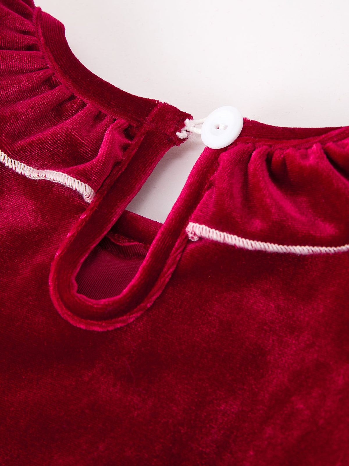 Burgundy velvet girls dress back detail featuring a white button, keyhole opening, and delicate white stitching along the neckline.
