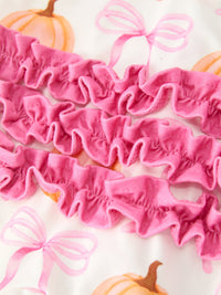 Pink ruffled trim details on baby girls pumpkin bow print fall romper with long sleeves and enclosed feet.