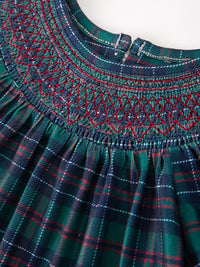 Festive green, navy, and red plaid girls dress featuring a detailed smocked yoke with red stitching and pleated skirt.