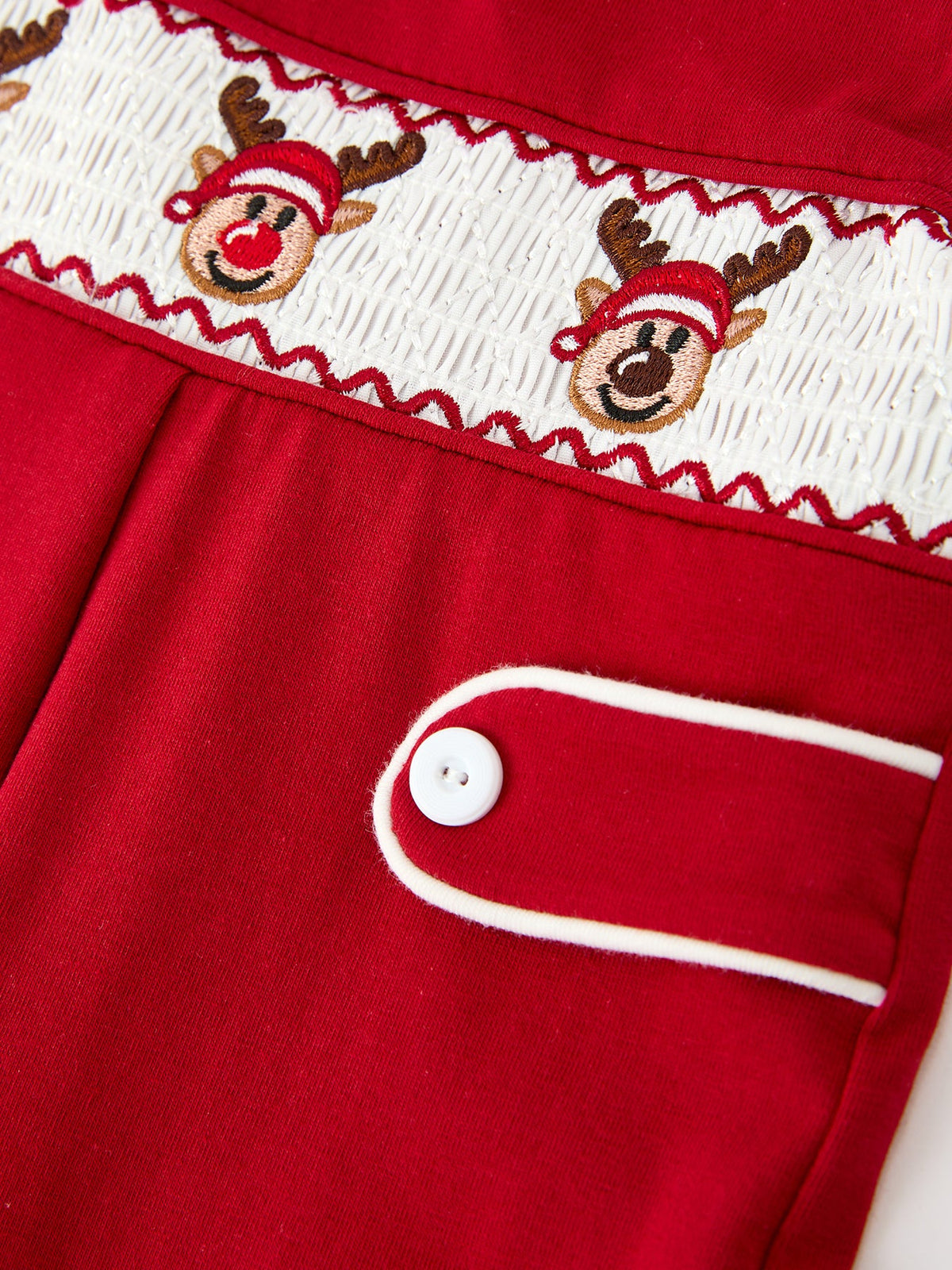 Red baby romper with embroidered reindeer on smocked chest, white contrast piping, and decorative shoulder button tab.