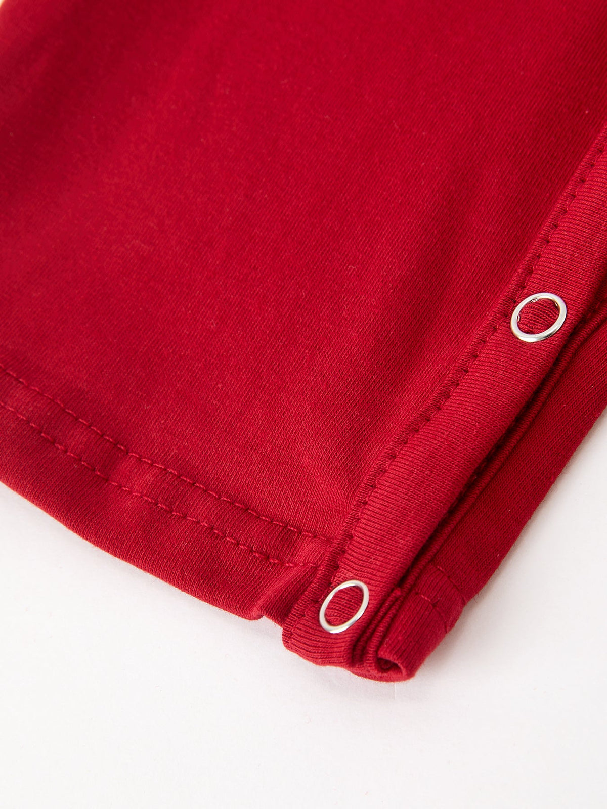 Red baby boysChristmas romper leg snap detail. Silver metal eyelets on festive red fabric with neat stitching for easy dressing.