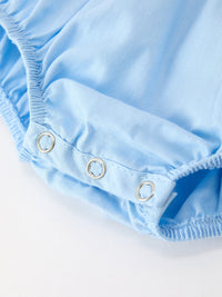 Close-up of metal snaps on light blue 100% cotton baby romper leg. Smocked Christmas nativity design with Peter Pan collar.