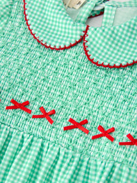Green plaid smocked baby romper bodice with red stitched Peter Pan collar and small red ribbon bows for festive holiday wear.