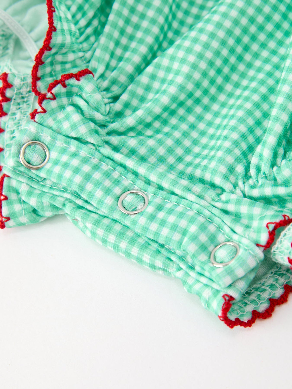 Green plaid bubble romper detail showing silver snap closures for easy diaper changes and red embroidered trim.