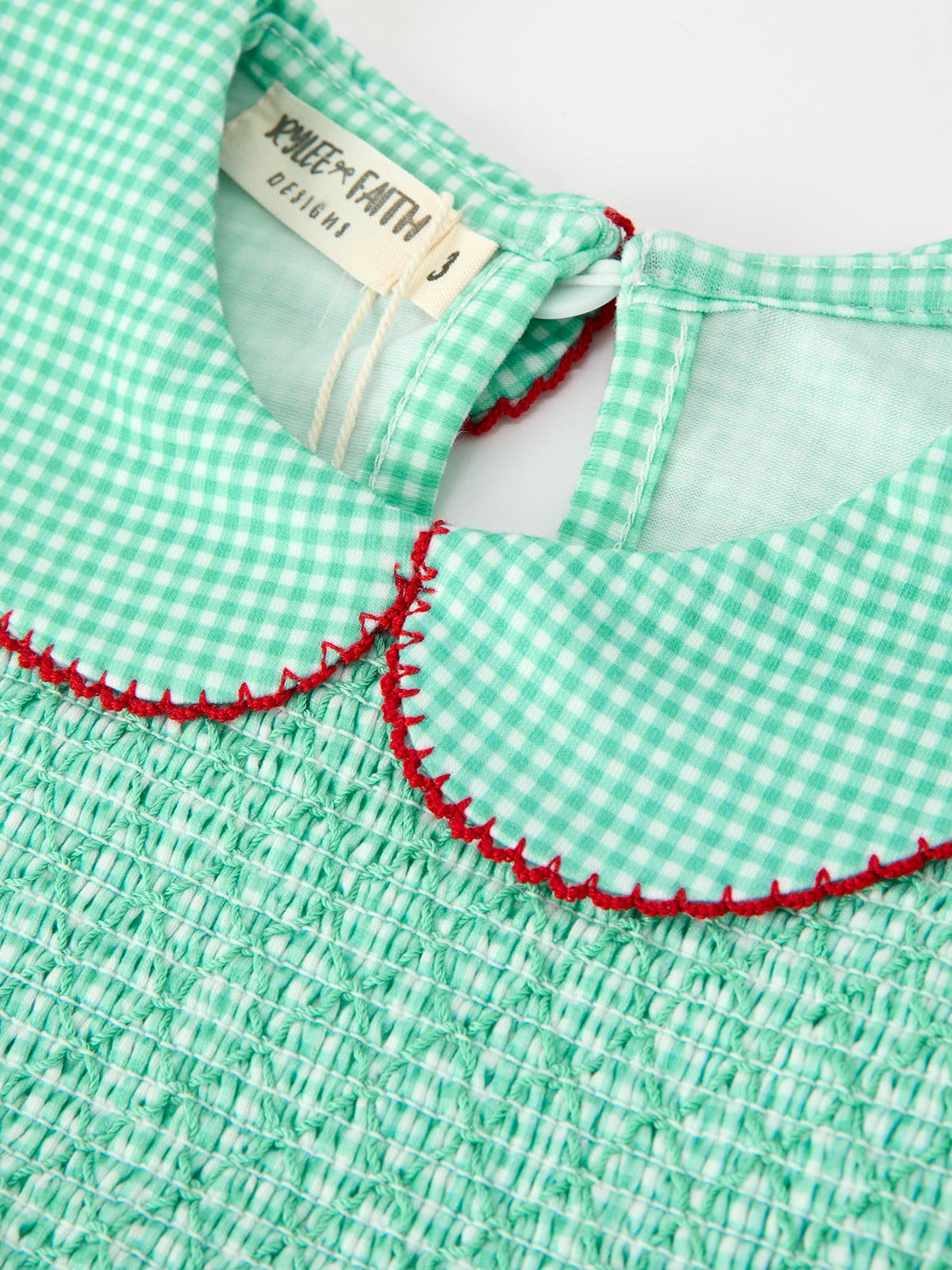 Green gingham girls dress with smocked bodice, Peter Pan collar trimmed in festive red stitching, and adjustable back tie.
