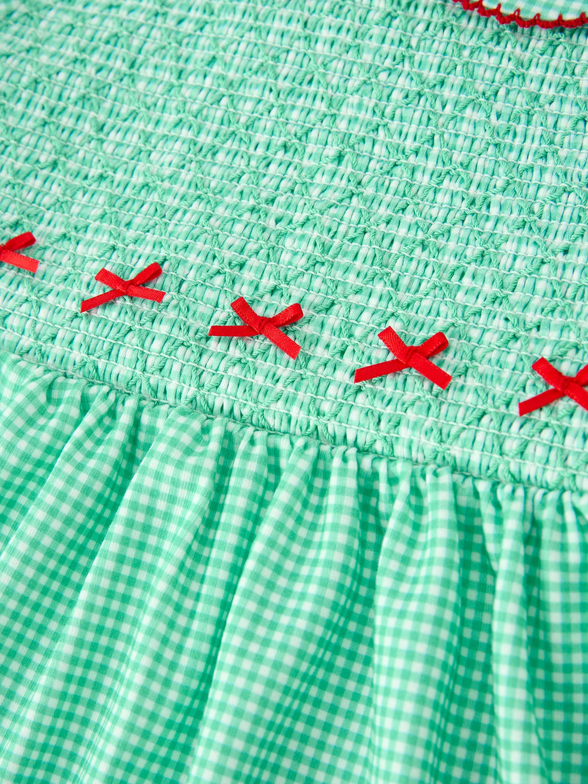 Green gingham dress bodice with smocked texture and small red ribbon bows. Festive Christmas girls outfit with vintage-inspired details.