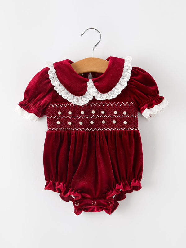 Burgundy velvet baby romper with pearl smocking, lace Peter Pan collar, puff sleeves, and ruffled leg openings.