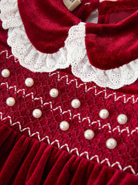 Burgundy velvet baby romper with pearl-accented smocking and white lace Peter Pan collar for Christmas.