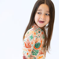 Young girl wearing The Second-Skin 2-Piece Long Sleeve Pajama, Desert Cactus beige, featuring colorful cactus print.