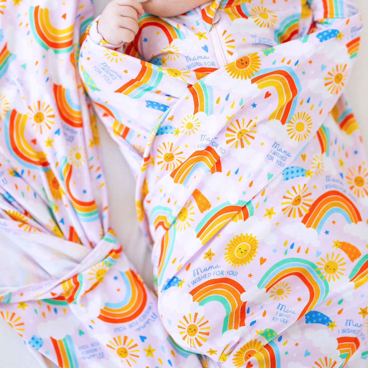 Close-up of The Forever Swaddle Blanket - Here Comes the Sunshine (Pink) being used to wrap a baby, displaying the playful rainbow and sun patterns for a nurturing and gentle embrace.