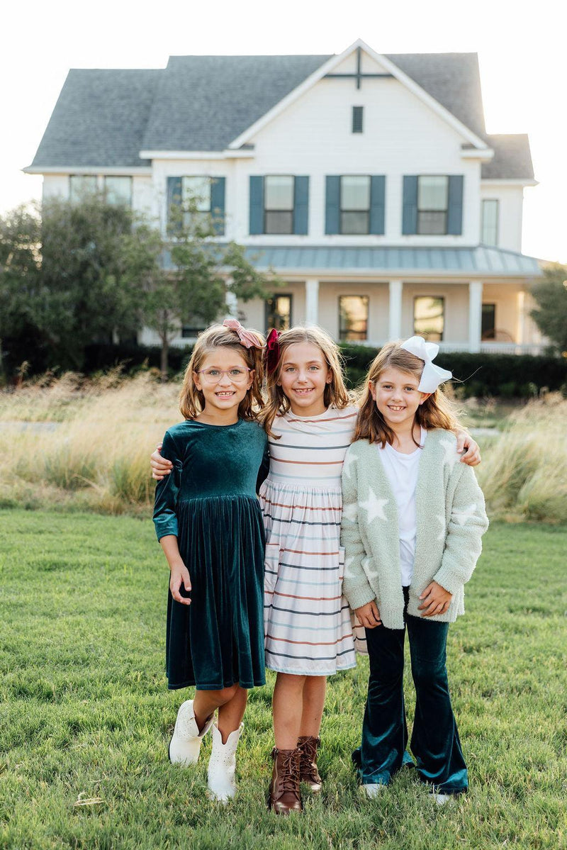 Three girls posing together outdoors, one wearing the Denim Blue Velvet Twirl Dress for Girls, surrounded by nature, highlighting playful moments.