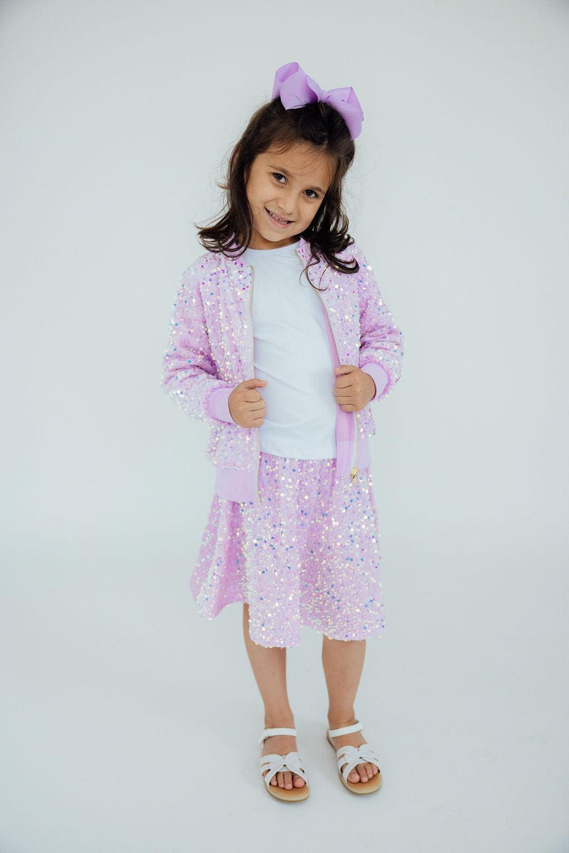 Young girl in a Lilac Velvet Sequin Jacket from Mila & Rose, posing with a smile, wearing a matching skirt and hair bow, perfect for capturing attention.