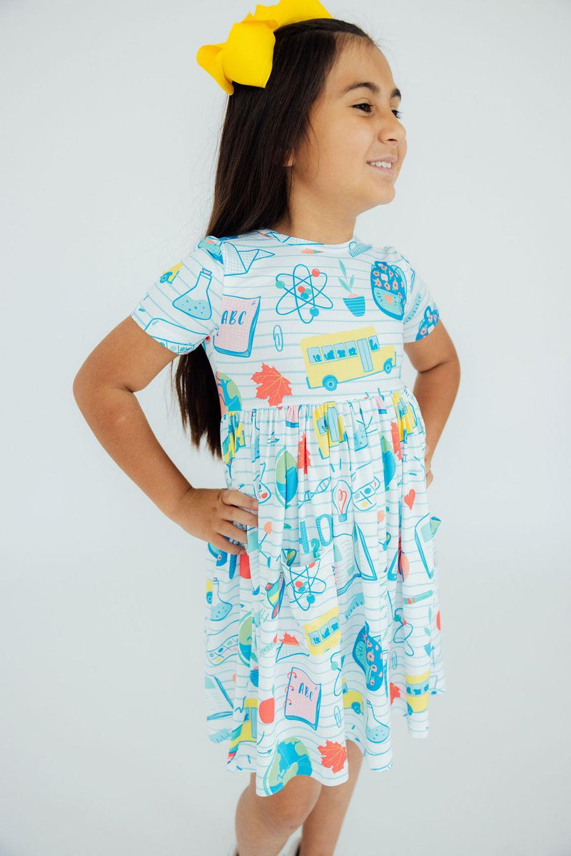 A girl confidently posing in the School Rules Short Sleeve Pocket Twirl Dress for Girls, showcasing its playful design and bright colors. The perfect twirl dress for girls for school and special occasions.