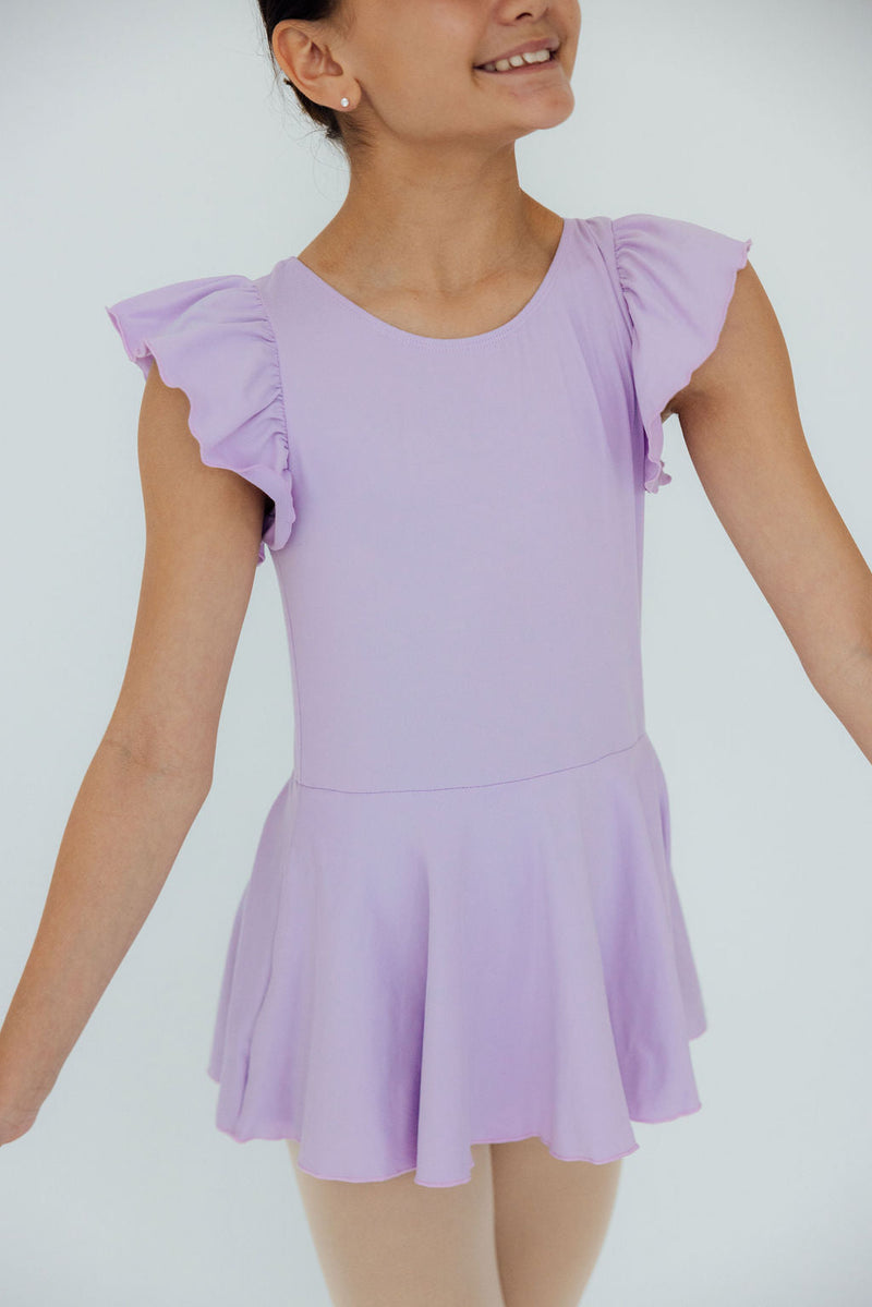 Smiling young dancer in a stylish Lavender S/S Twirl Leotard by Mila & Rose, twirling with joy, flaunting fluttery sleeves and a delightful lavender hue.