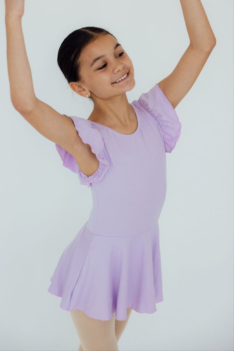 Joyful young dancer striking an elegant pose in the Lavender S/S Twirl Leotard by Mila & Rose, displaying delightful ruffled sleeves and a twirl-ready design.