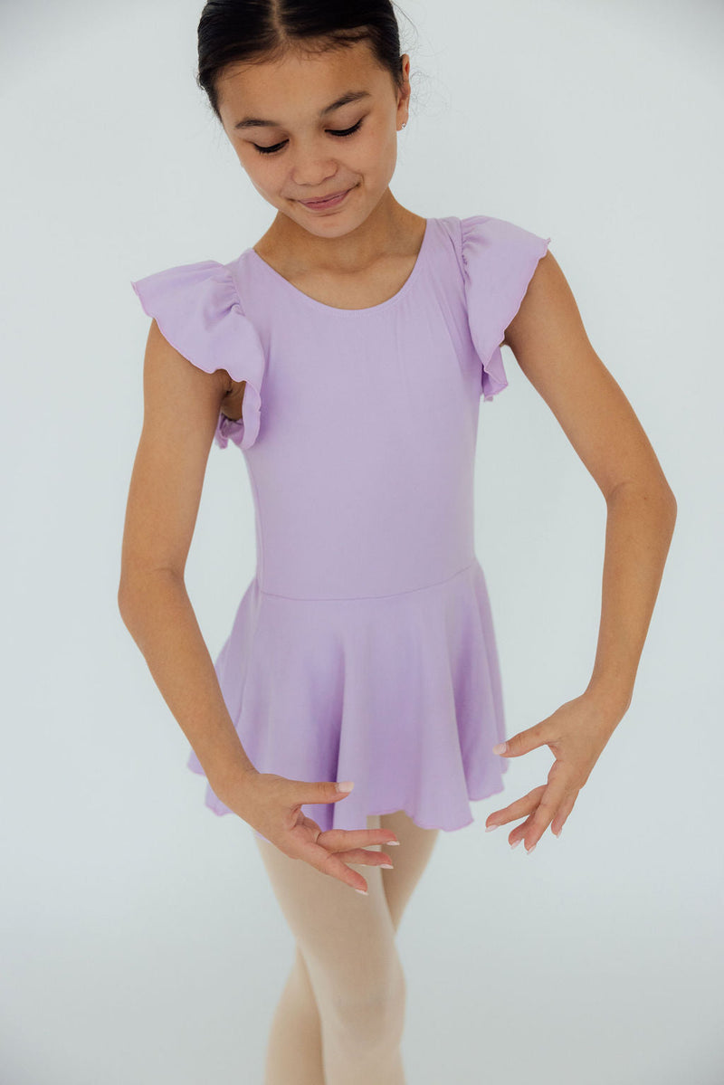 A young ballerina beautifully poses in the Lavender S/S Twirl Leotard by Mila & Rose, showcasing ruffled sleeves and a playful skirt, perfect for twirls and spins.