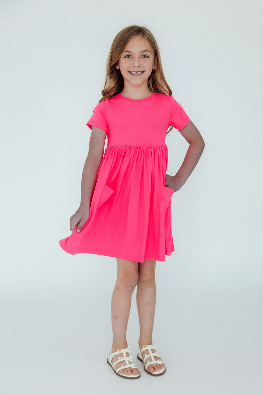 Girl wearing the Neon Pink S/S Pocket Twirl Dress by Mila & Rose, smiling and posing with a playful twirl stance.
