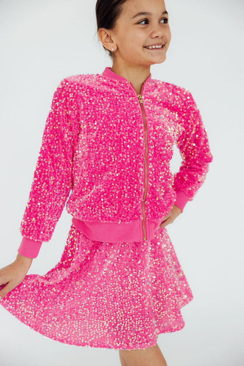 A girl joyfully flaunts her Pink Velvet Sequin Jacket, complete with a twirl in her matching skirt. This outfit screams fun and elegance for any occasion!