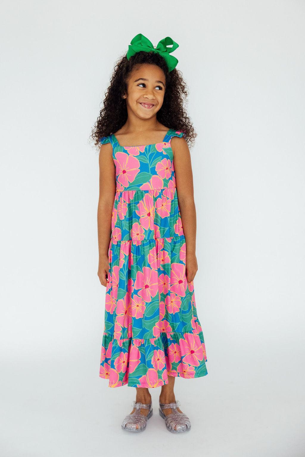 A joyful girl wearing the Luau Floral Ruffle Maxi Dress with vibrant pink and green floral patterns, perfect for summer fun!