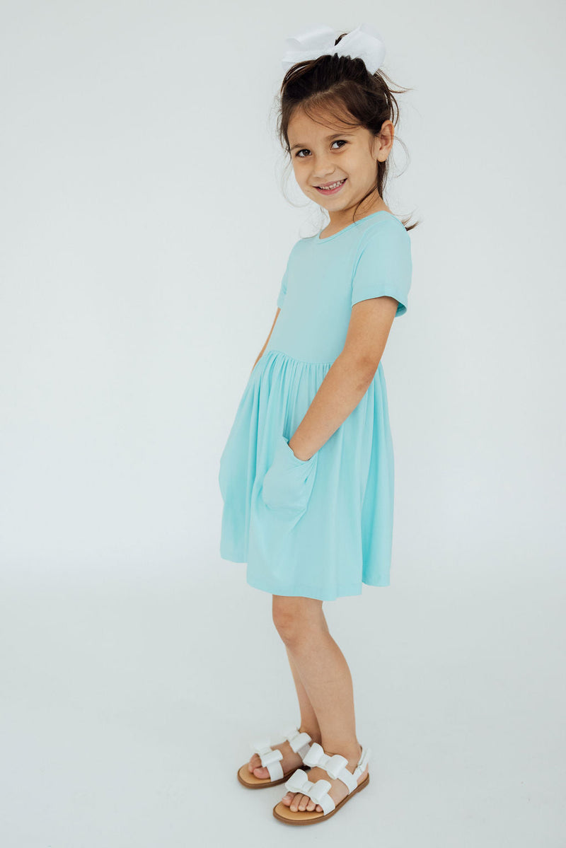 Aqua S/S Pocket Twirl Dress worn by a smiling girl, showcasing its stylish design and functional pockets.