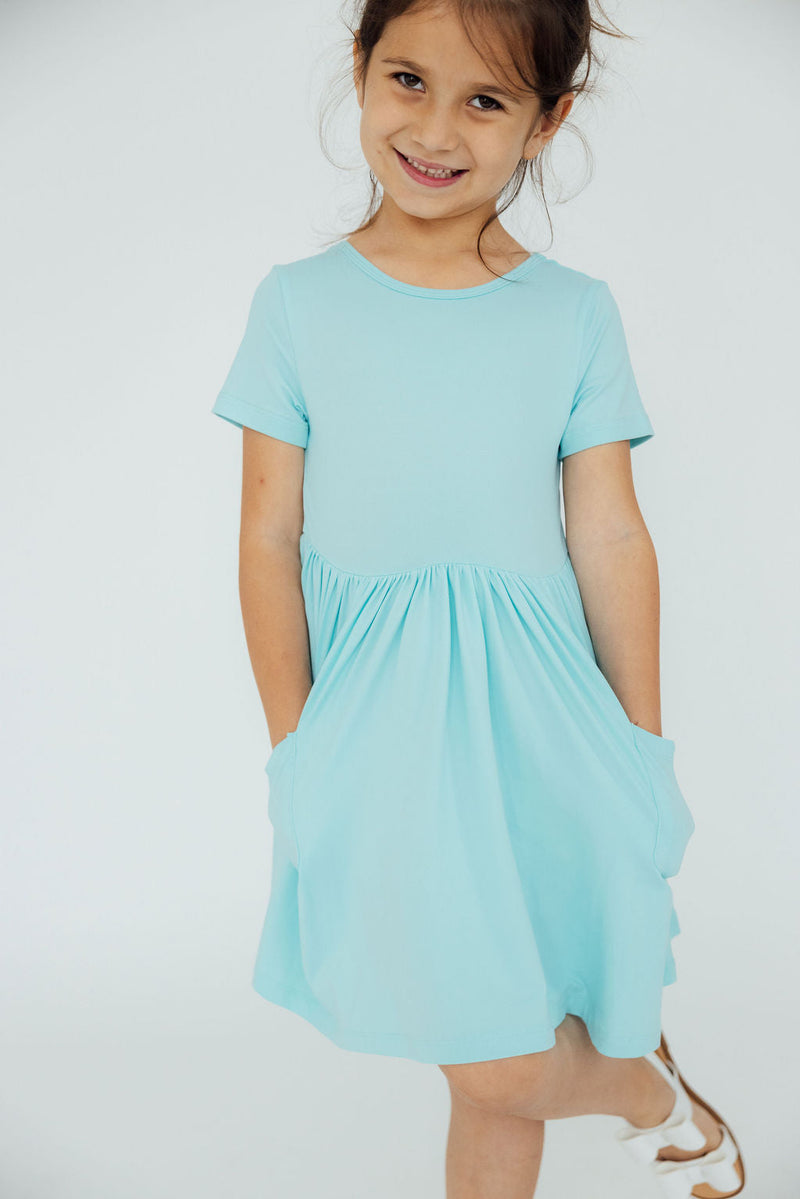 Front view of a girl in an Aqua S/S Pocket Twirl Dress, highlighting the elegant silhouette and soft fabric.