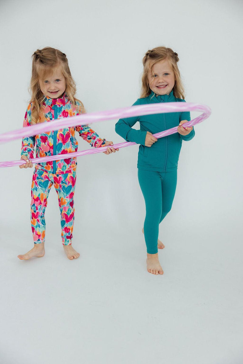 Two smiling girls playing together with hula hoops, both in stylish outfits including the Heart Hustle Full-Zip Ruffle Girls Active Jacket, perfect for active play in their girls active jackets.