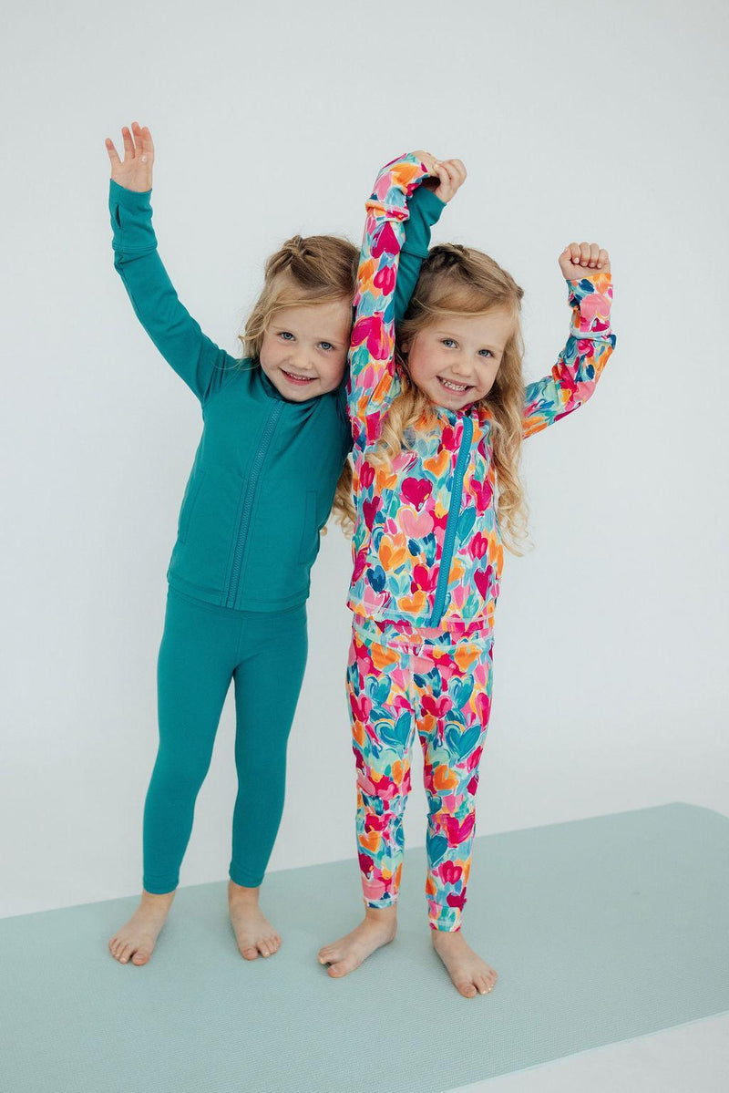 Joyful girls celebrating in vibrant outfits, one in floral and the other in Turbo Teal Active Leggings for Girls, perfect for active play and stylish adventures.