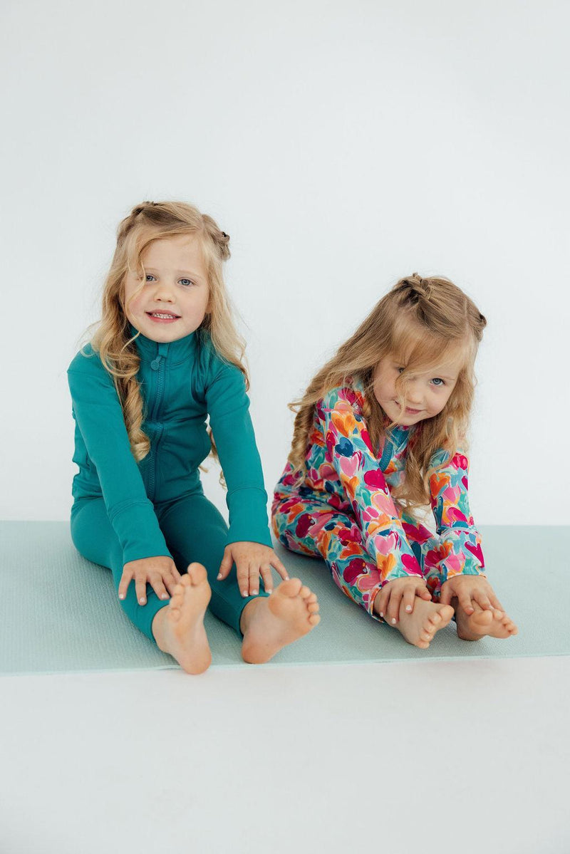 Two girls stretching on a mat, showcasing the Turbo Teal Full-Zip Ruffle Girls Active Jacket as part of their girls activewear collection.