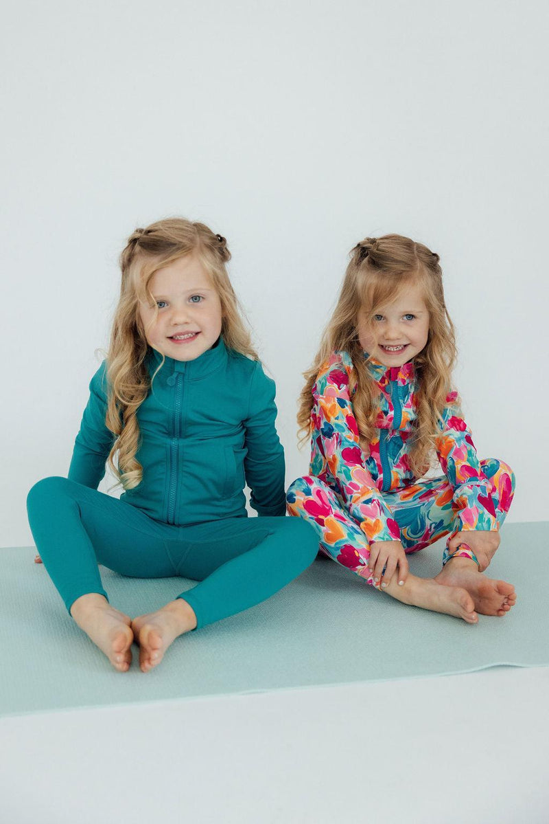 Two girls sitting on a mat, one in the Turbo Teal Full-Zip Ruffle Girls Active Jacket, embodying comfort in girls activewear jackets.