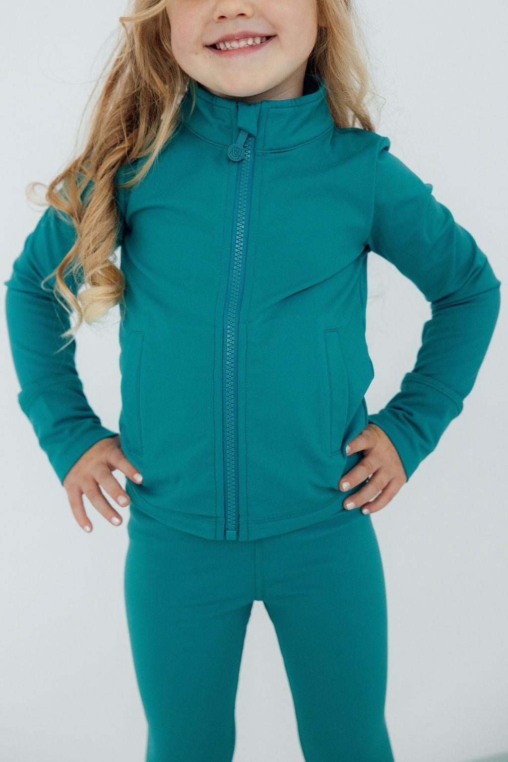 Smiling girl showcasing the Turbo Teal Full-Zip Ruffle Girls Active Jacket, part of the girls activewear jacket collection.