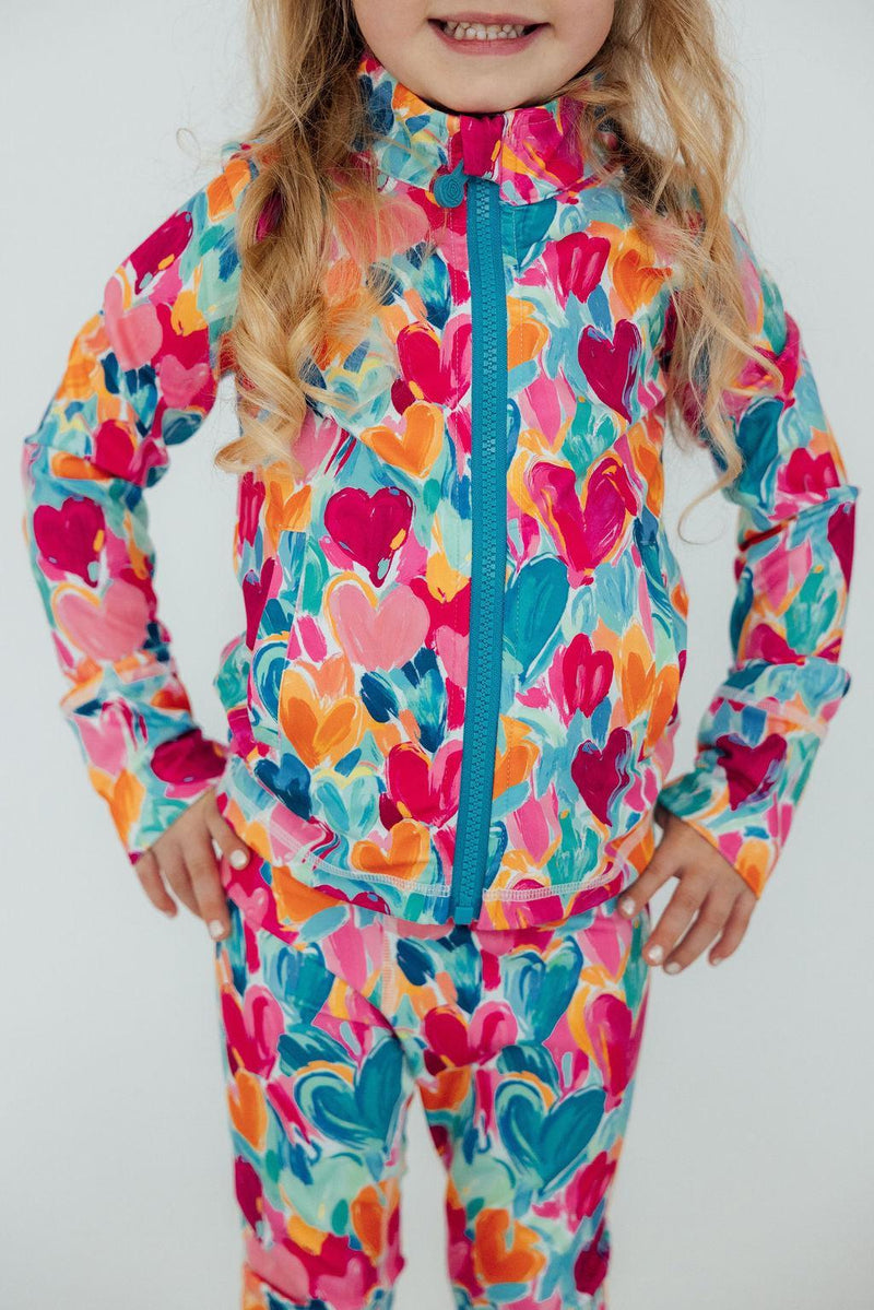 A close-up of a girl wearing the Heart Hustle Full-Zip Ruffle Girls Active Jacket in vibrant Turbo Teal, posing confidently and showing off the colorful design of her girls active jacket.