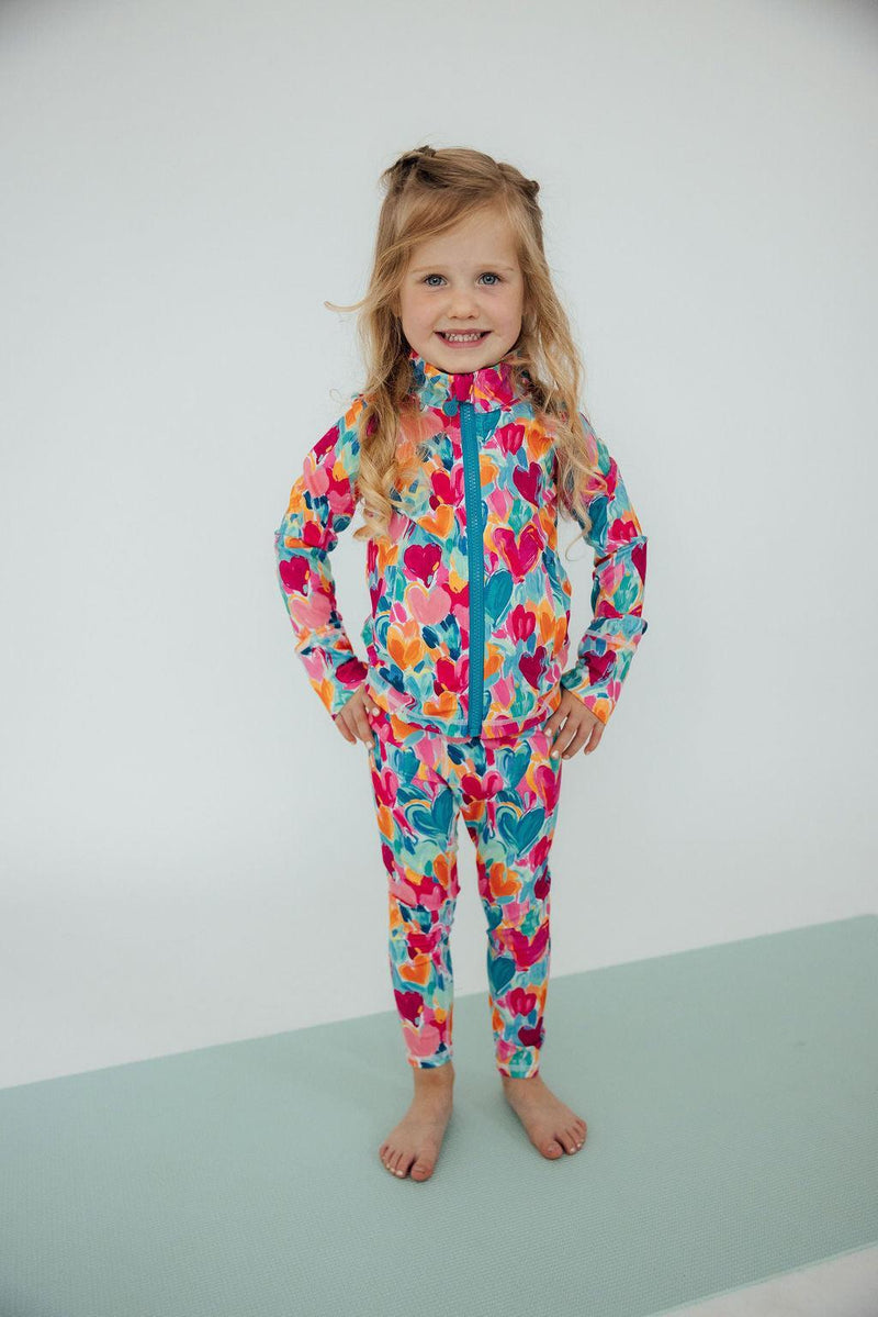 A joyful girl posing in the Heart Hustle Full-Zip Ruffle Girls Active Jacket, showing off her stylish and comfortable outfit, ideal for an active lifestyle in girls active jackets.