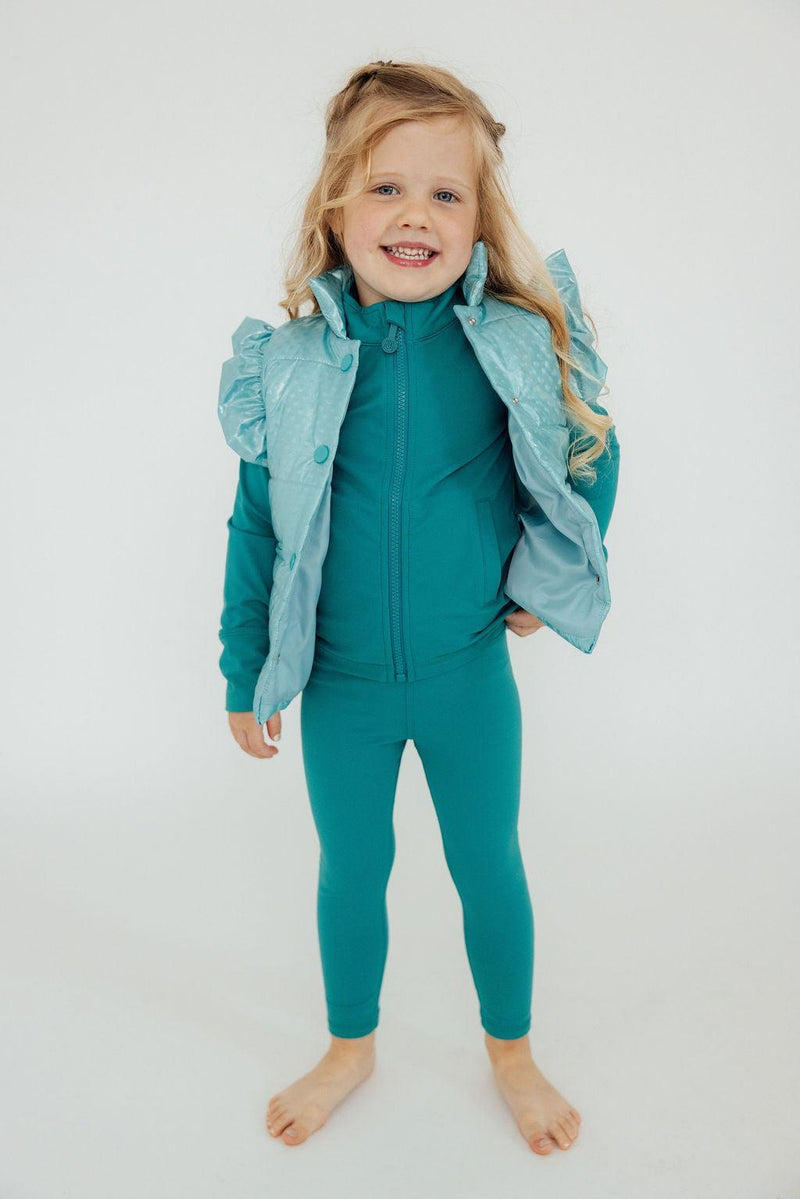 Cheerful girl in a Turquoise Dot Puffer Vest by Mila & Rose, posing with a radiant smile and showcasing a cute and cozy winter outfit.