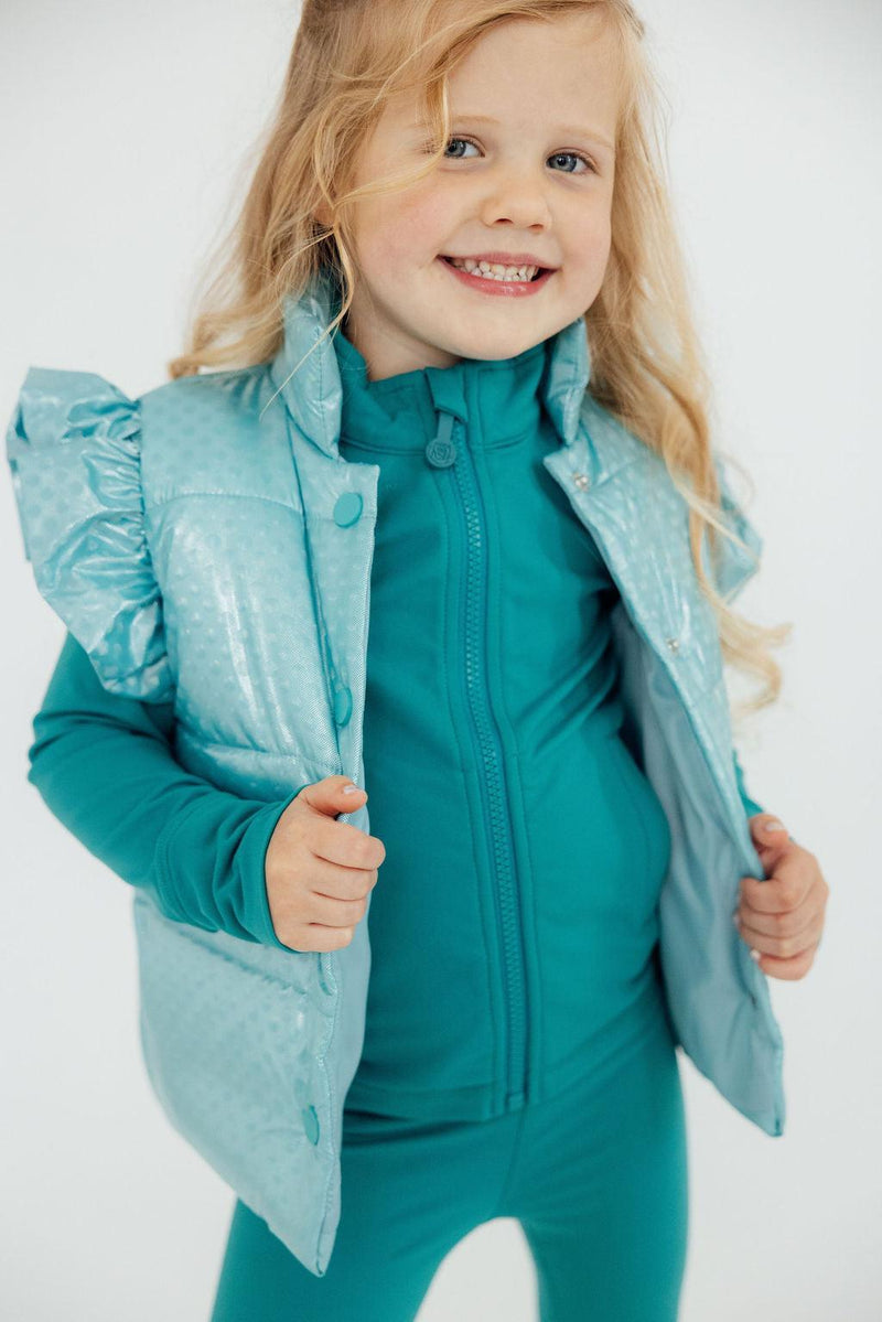 A cheerful child wearing a Turquoise Dot Puffer Vest by Mila & Rose, showcasing a playful and stylish look perfect for winter layering.