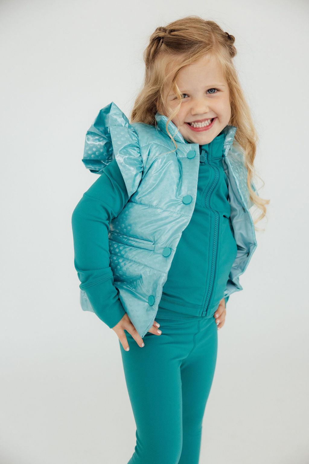 Smiling girl wearing a Turquoise Dot Puffer Vest by Mila & Rose, posing confidently with her hands on her hips.
