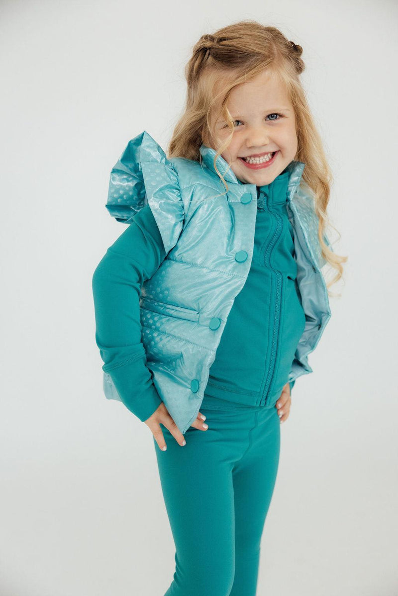 Smiling girl wearing a Turquoise Dot Puffer Vest by Mila & Rose, posing confidently with her hands on her hips.