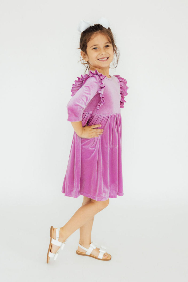 Charming girl in the Carnation Pink Velvet Ruffle Twirl Dress by Mila & Rose, happily twirling with a joyful expression and cute accessories.