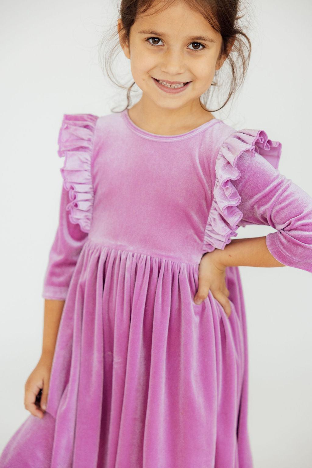 Girl wearing the Carnation Pink Velvet Ruffle Twirl Dress by Mila & Rose, showcasing ruffles on the sleeves and a playful pose.