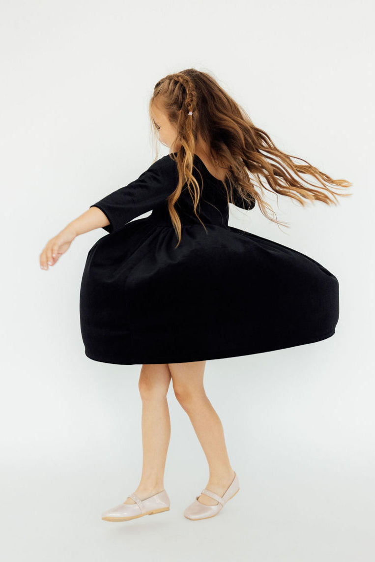 Girl twirling in the SALE Black Velvet Twirl Dress from Mila & Rose®, highlighting the dress's full skirt and twirl-friendly design.