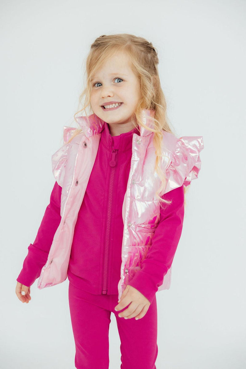 A cheerful child sporting the Pink Iridescent Puffer Vest from Mila & Rose ®, showcasing its shiny finish. Perfect for winter warmth and style!