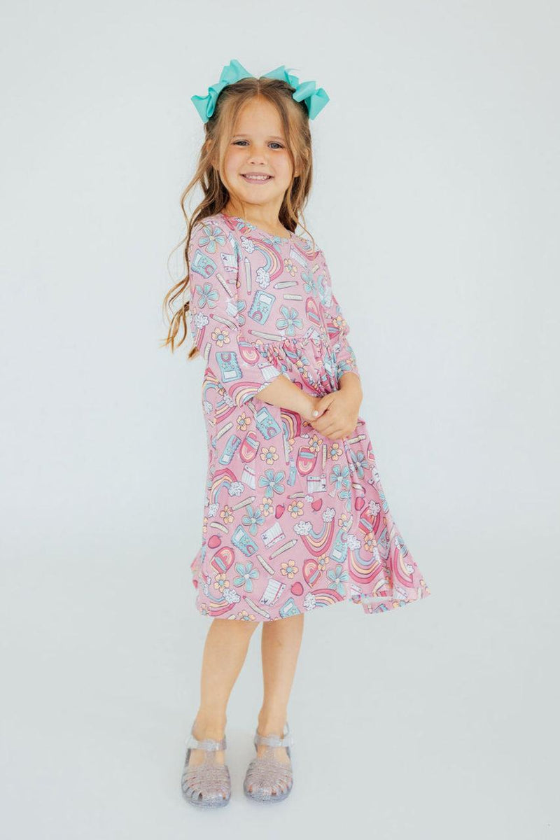 A cheerful girl smiling while wearing the Dream Big Little One 3/4 Pocket Twirl Dress by Mila & Rose®, showcasing the unique patterns and a cute hairstyle.